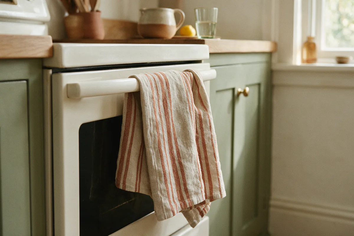 A rust and oat striped linen towel hanging from an oven handle.