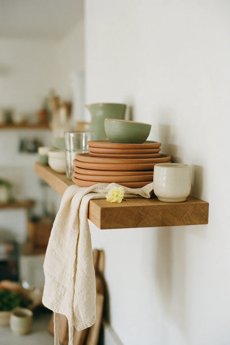 Side view of a solid oak shelf with a stack of dinner plates sitting on it.