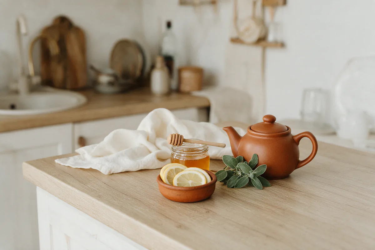 A bowl of lemon slices, a jar of honey and fresh mint beside a teapot.