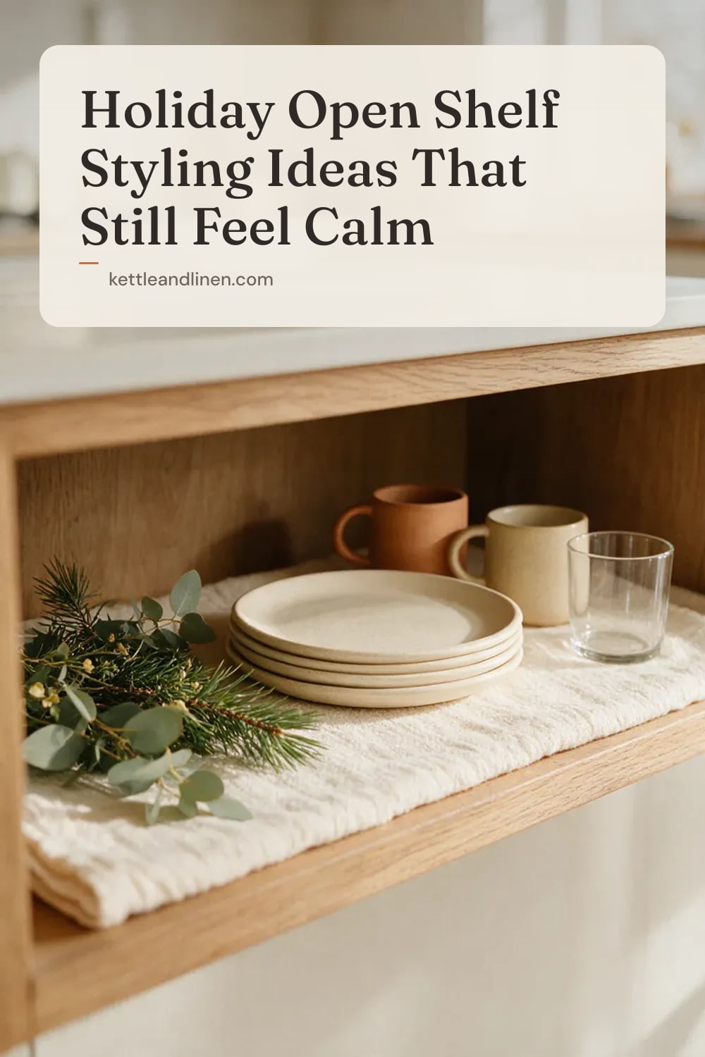 A wooden kitchen shelf with fresh pine sprigs beside cream plates and mugs.